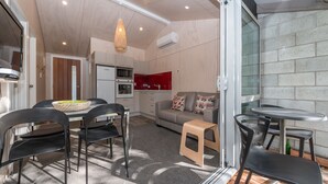 Een moderne keuken met een magnetron, oven en een rode achterwand. Er is een eethoek met een tafel en stoelen, en een klein krukje.