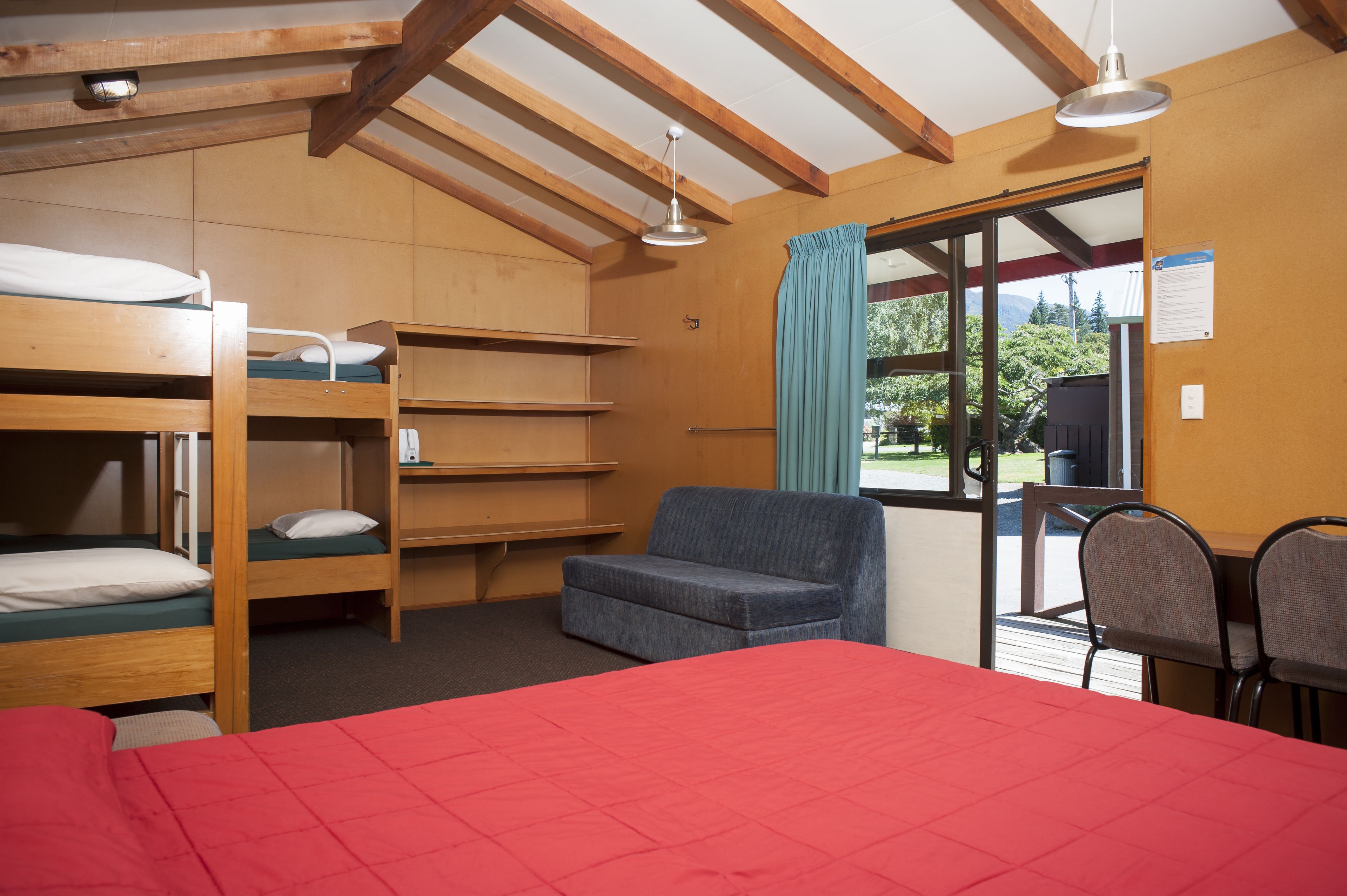A dormitory room with bunk beds, a red bed, a blue chair, and a table with chairs.