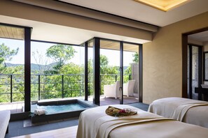 Un cuarto de spa con un jacuzzi, dos camillas de masaje y vistas a la vegetación.