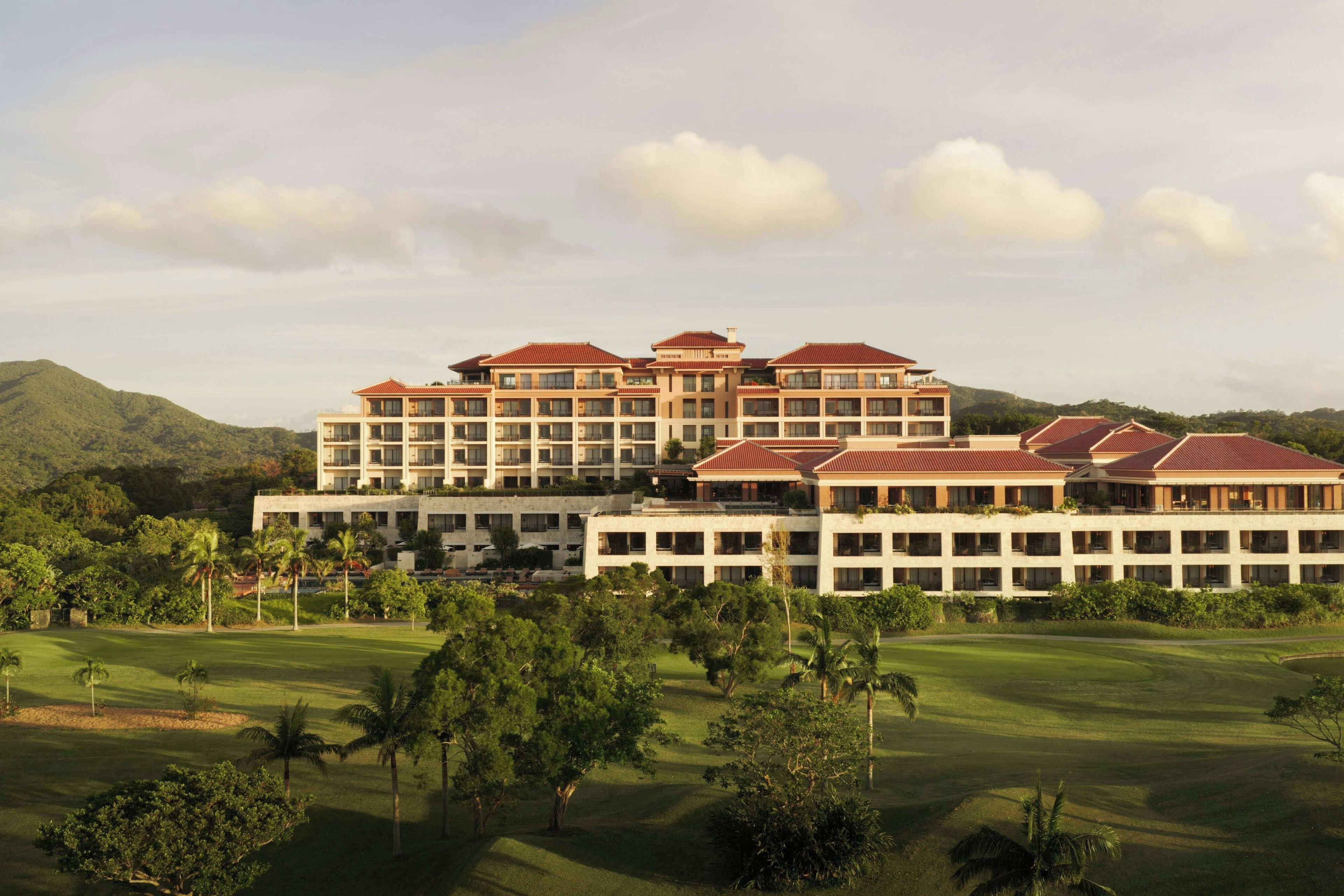 A multi-story hotel with a modern architectural design, featuring a flat roof and large windows. The hotel is surrounded by lush greenery and a well-maintained golf course.