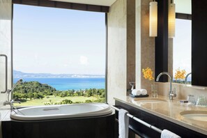 A bathroom with a large bathtub, two sinks, and a view of a golf course and sea.