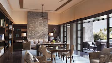 A spacious living area with a dining table, comfortable seating, a large stone wall, and a view through large windows.