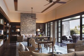 Un salón amplio con mesa de comedor, asientos cómodos, un gran muro de piedra y vistas a través de grandes ventanales.