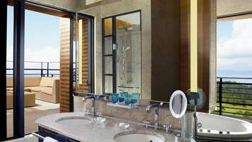A modern bathroom with dual sinks, a large mirror, and a bathtub. It features a glass shower enclosure and a view of the outdoors.