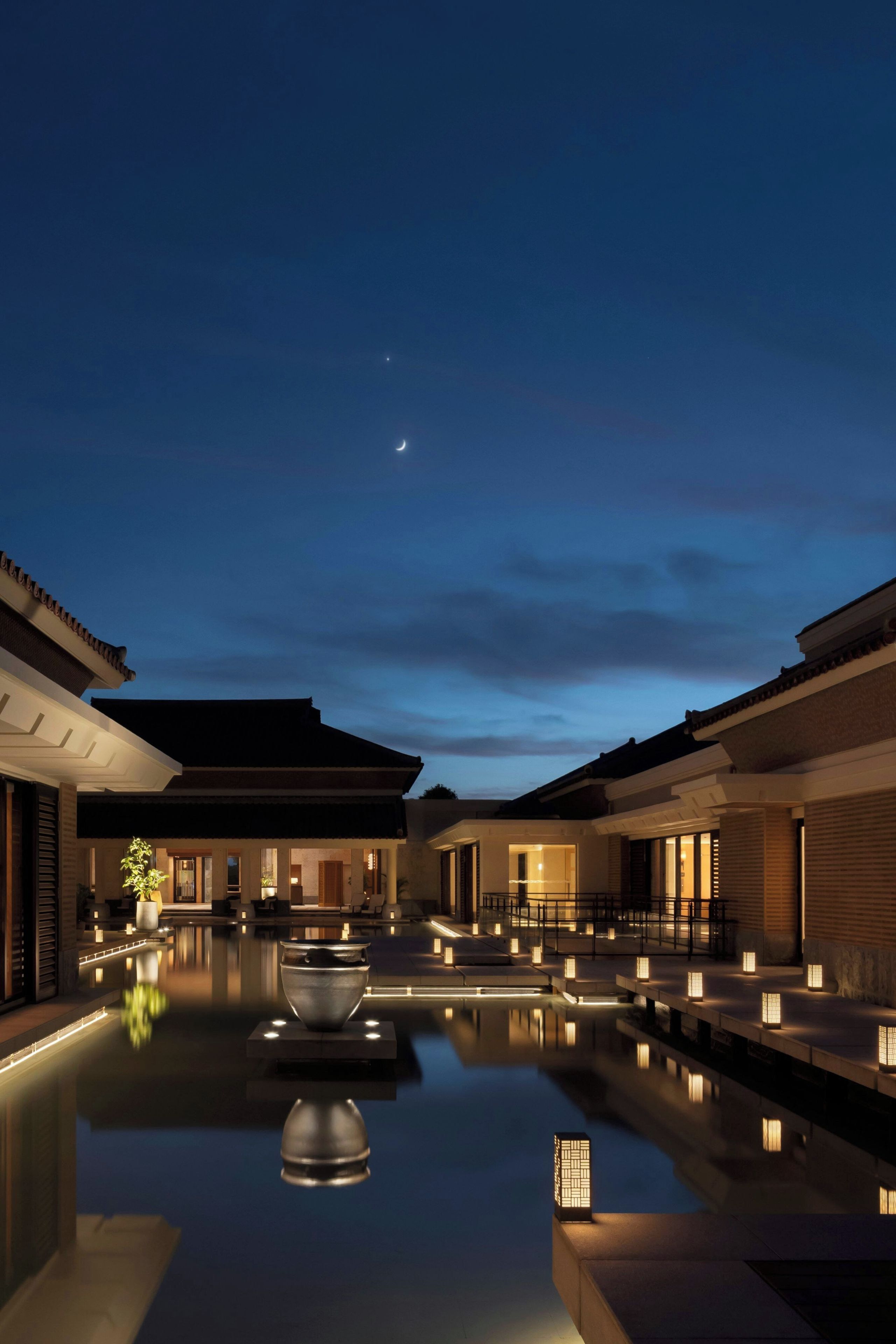 A serene courtyard with a reflective pool, traditional architecture, and ambient lighting.