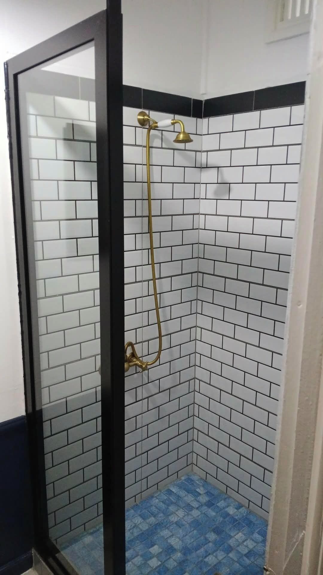 A shower with a glass door, white and black tiled walls, and a blue-tiled floor.