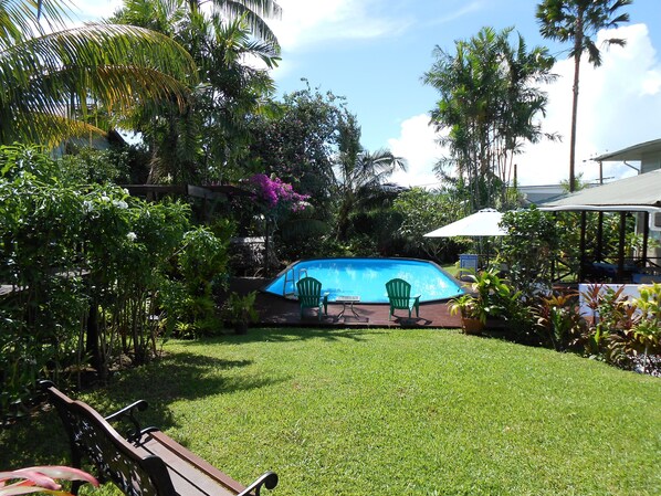 Un jardin avec une piscine, une pelouse verdoyante et diverses plantes tropicales.