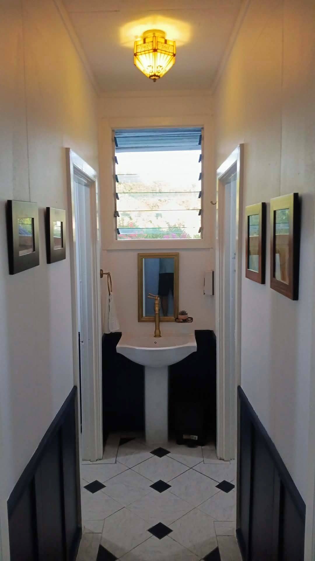 A narrow hallway with a white sink, a mirror, and framed pictures on the walls.