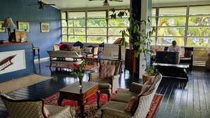 A spacious living room with a large window, a ceiling fan, and a variety of seating options. - The Samoan Outrigger Hotel (Apia)