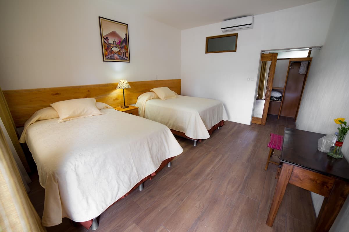Quarto de hotel com duas camas, cabeceira de madeira, uma mesa e uma cadeira.