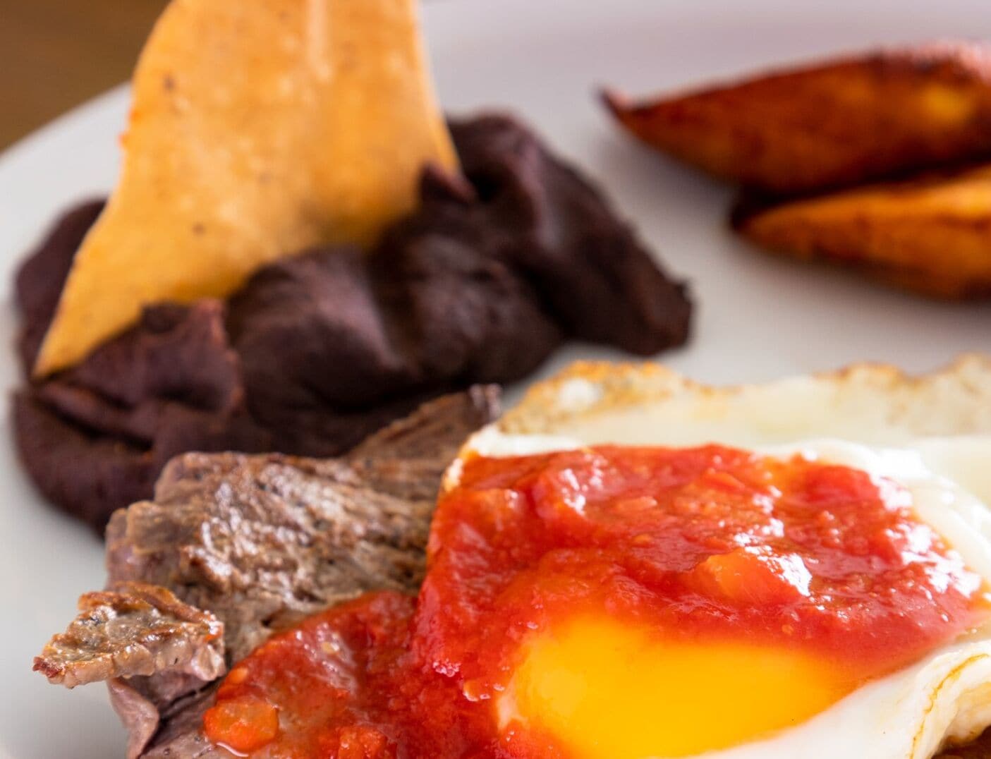 A plate with a fried egg, black beans, beef, and fried plantains.