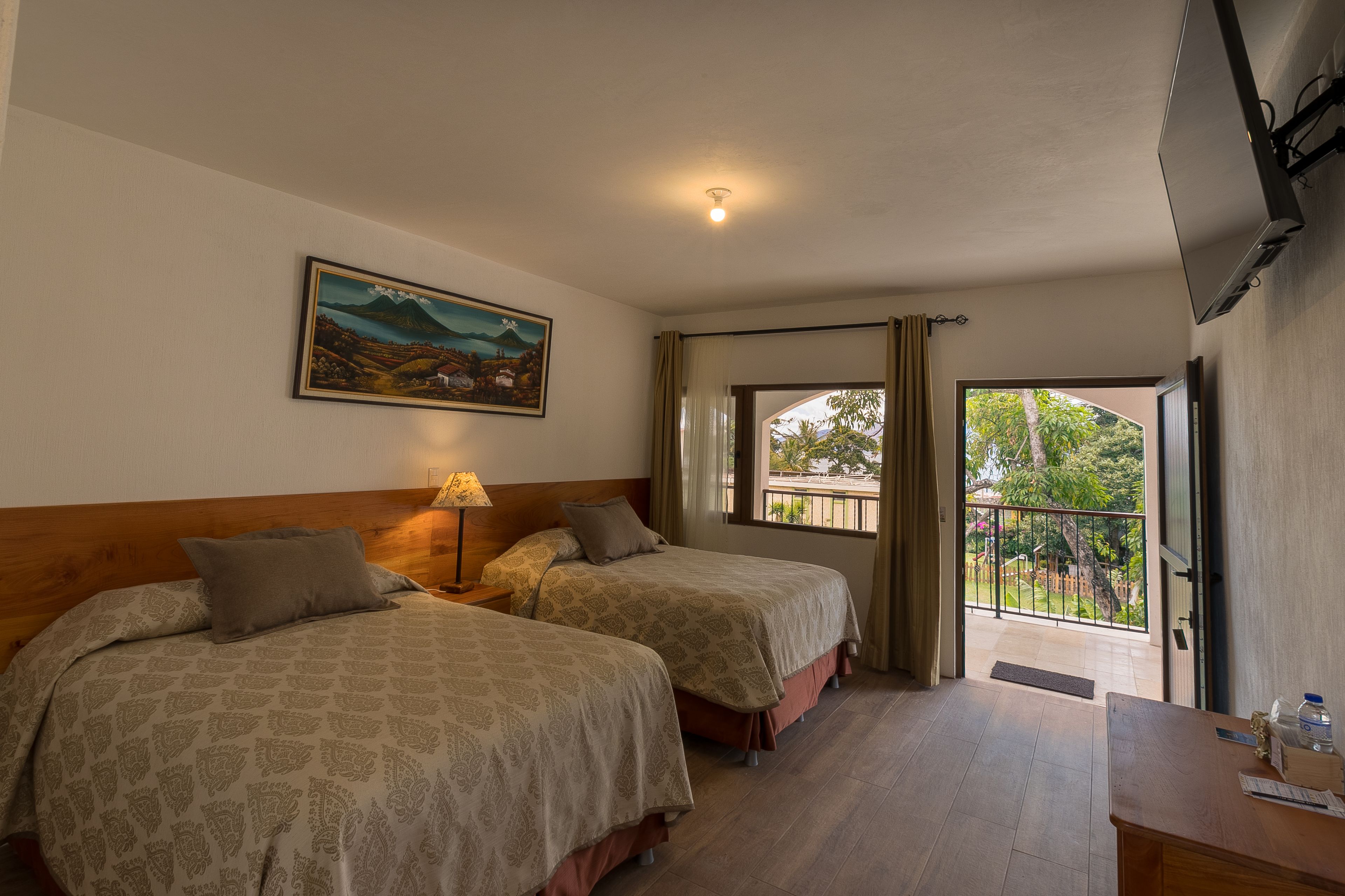 Habitación de hotel con dos camas, un cuadro en la pared, un escritorio con lámpara y un balcón con vistas.