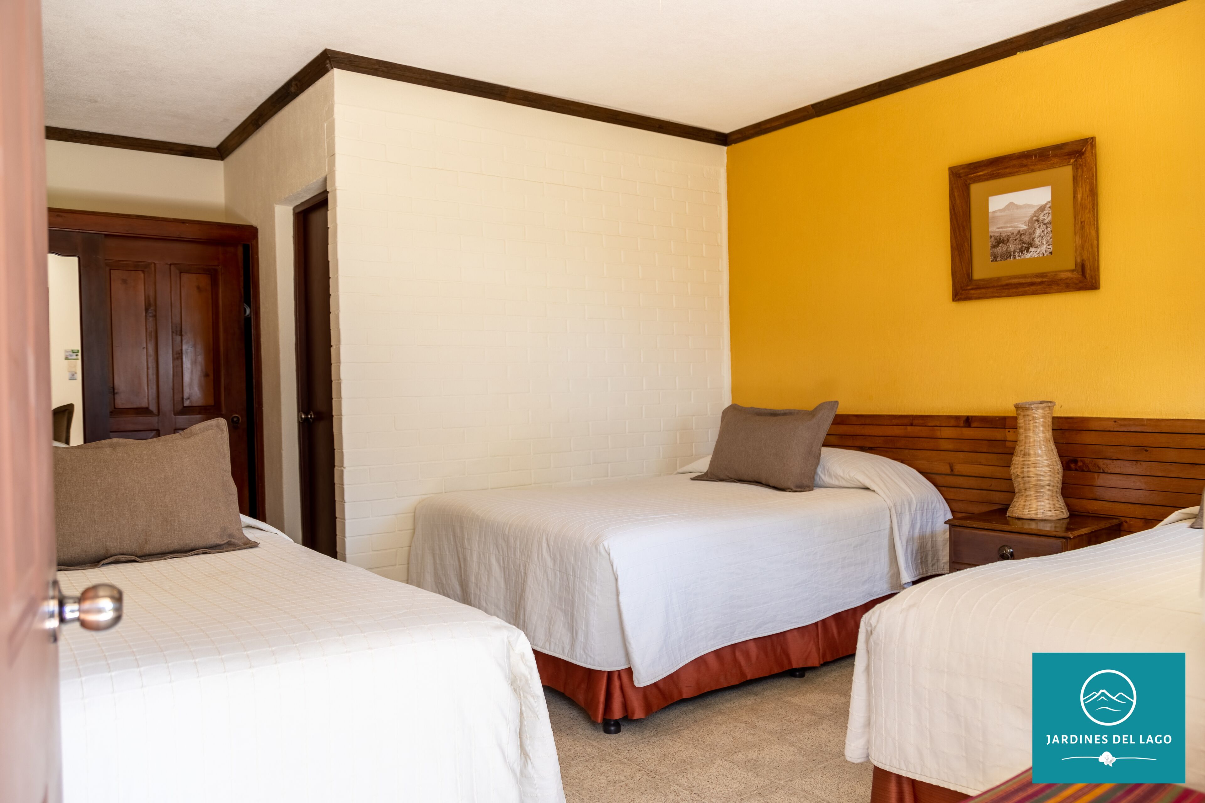 Habitación de hotel con dos camas, un cabecero de madera, un cuadro en la pared y una puerta.