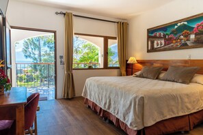 A hotel room with a large bed, a balcony with a view of the sea, and a painting on the wall.