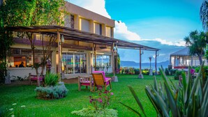 Un hôtel doté d’un espace extérieur couvert avec des sièges, d’un jardin avec différentes espèces de plantes et d’une vue sur la mer.
