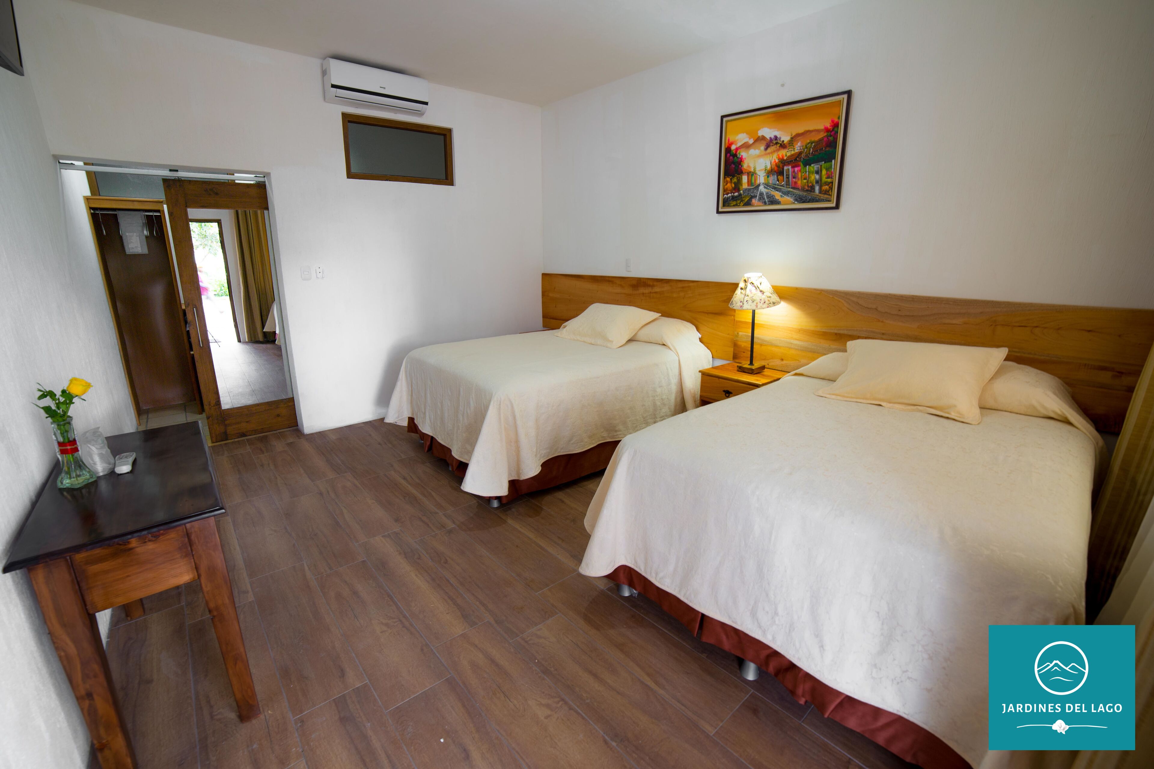 Ein Hotelzimmer mit zwei Betten, einem hölzernen Kopfteil, einem Nachttisch mit Lampe, einem kleinen Tisch mit Blumenvase und einem Bild an der Wand.