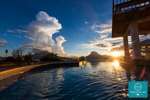 A pool area with a view of the sunset and mountains in the background.