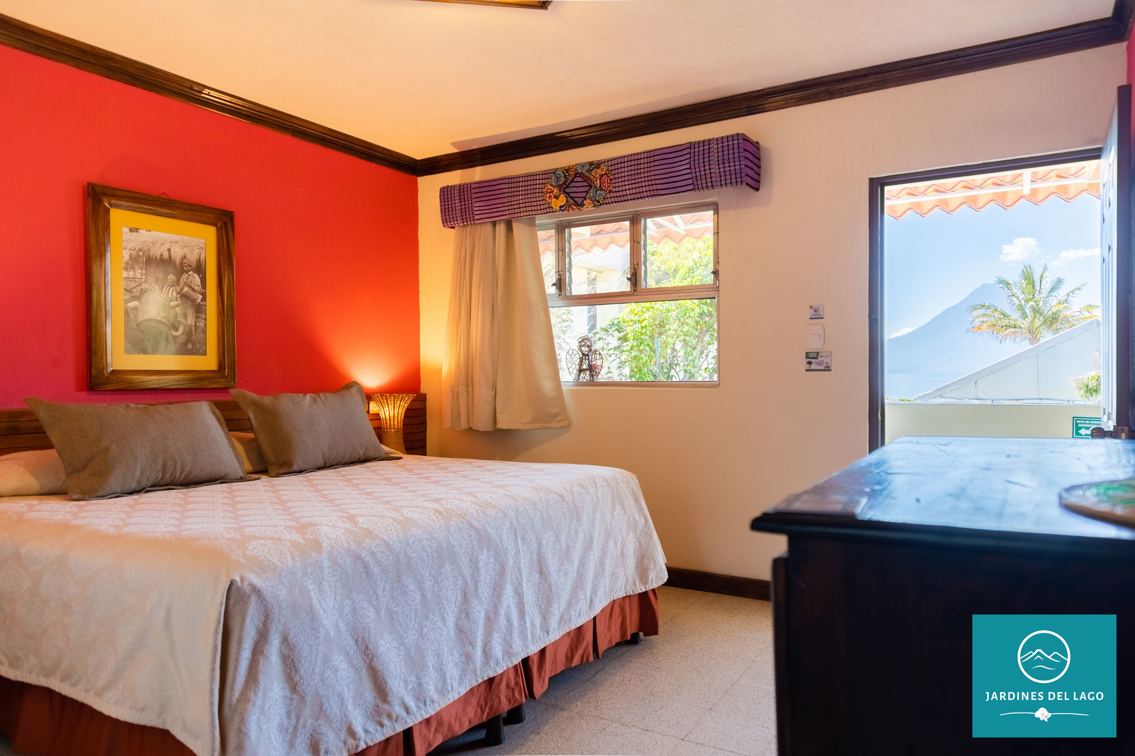 A hotel room with a bed, a window with curtains, a framed picture on the wall, and a view of the outside.