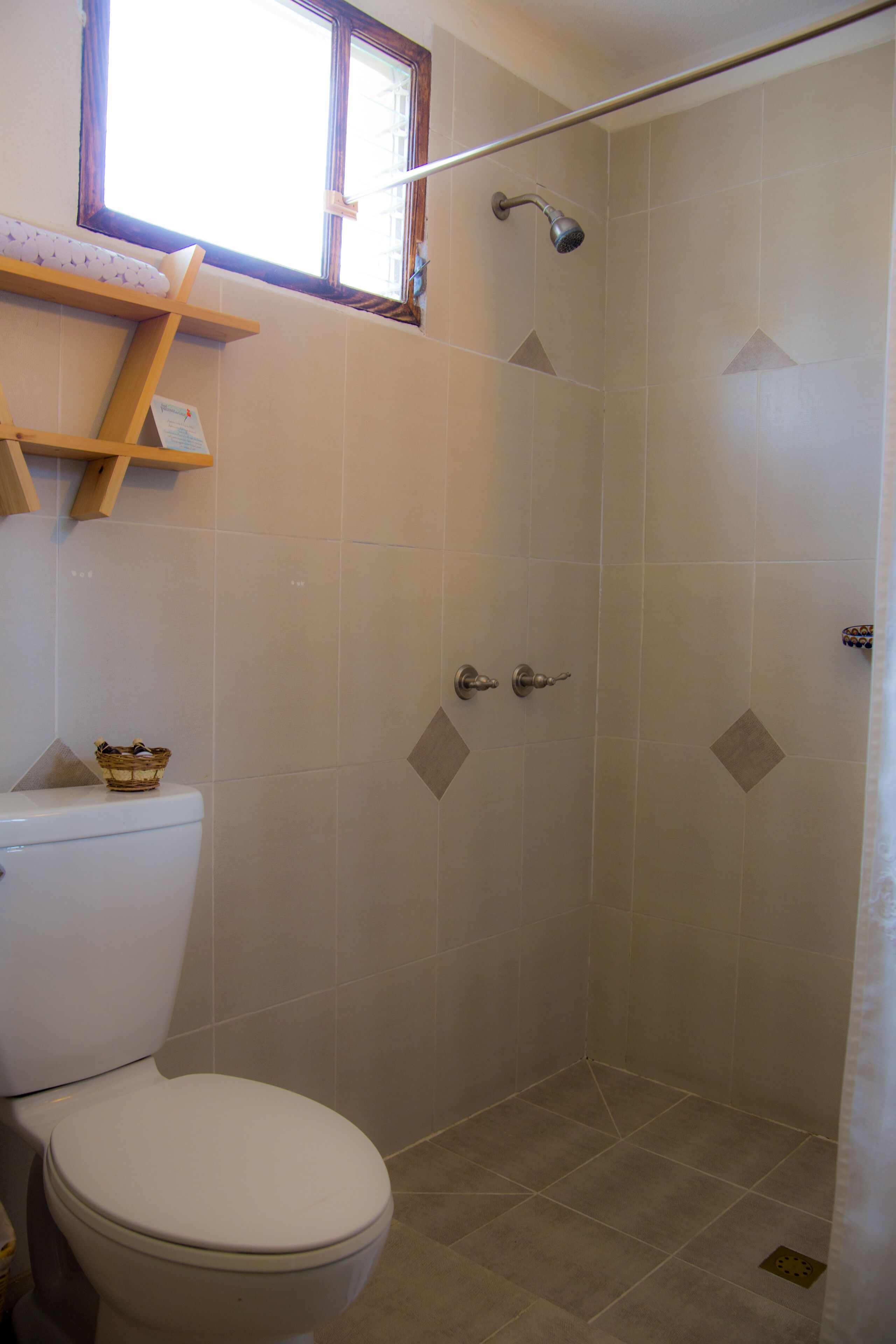 Un baño con inodoro, ducha y ventana sobre el inodoro.