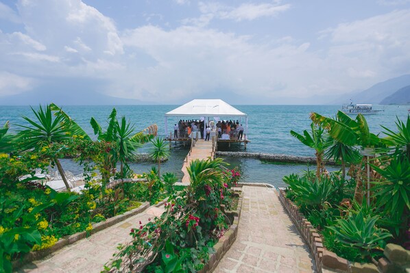 A white tent with a crowd, surrounded by lush greenery and a body of water. - Hotel y Centro de Convenciones Jardines del Lago (Panajachel)