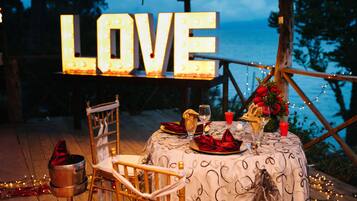 Ein romantisches Essensarrangement im Freien mit einem 'LOVE'-Schild, Tisch gedeckt mit roten Servietten und Blick aufs Meer.