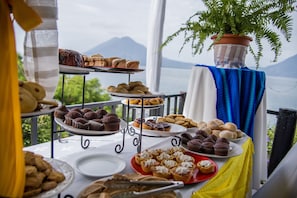 Una mesa de buffet con diversas pastelerías y postres, con un paisaje montañoso de fondo.