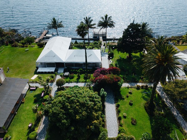An aerial view of a resort with a large white building, palm trees, and a pathway leading to the water.