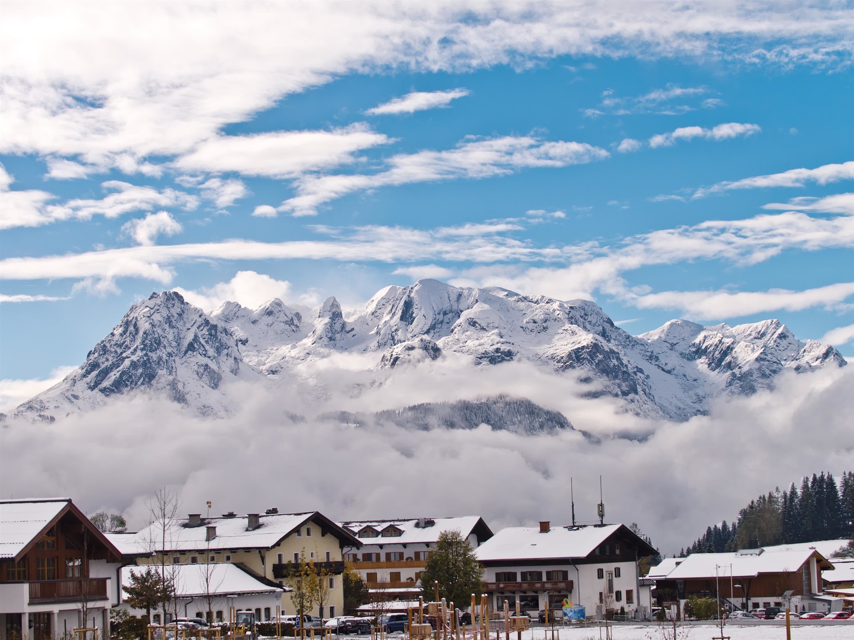 Un village de montagne aux bâtiments couverts de neige, offrant une vue sur des sommets enneigés.