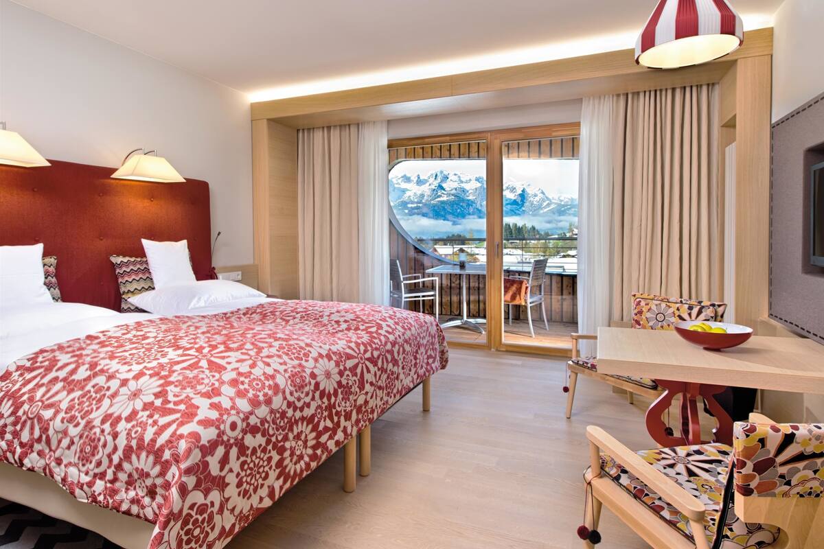 A hotel room with a bed, a dining table, and a view of mountains.