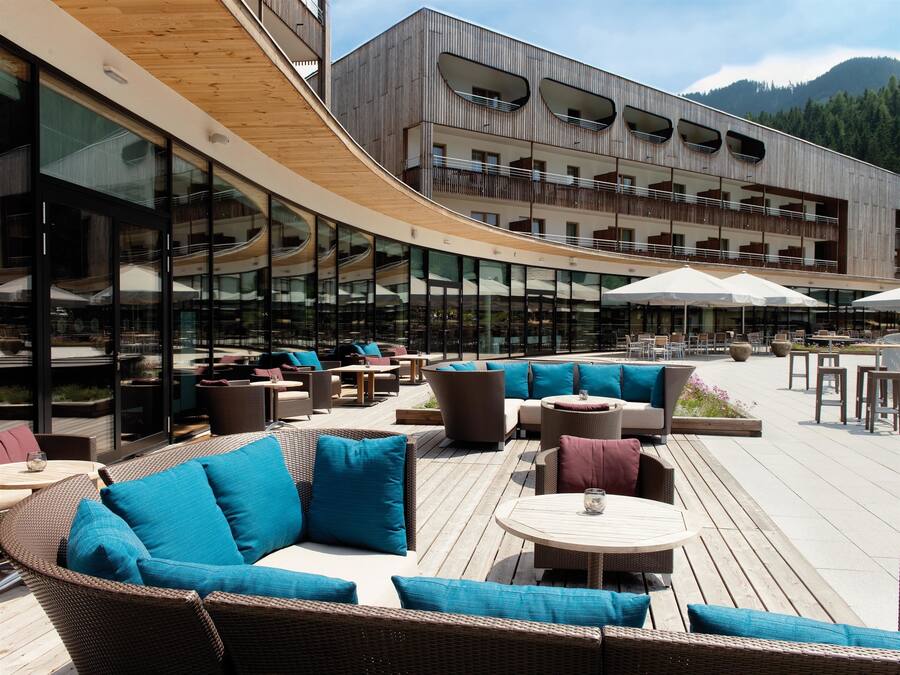 An outdoor seating area with wicker furniture and umbrellas, overlooking a modern building with large windows and balconies.