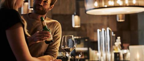 A man holding a bottle and a glass at a bar with a modern interior and pendant lighting.
