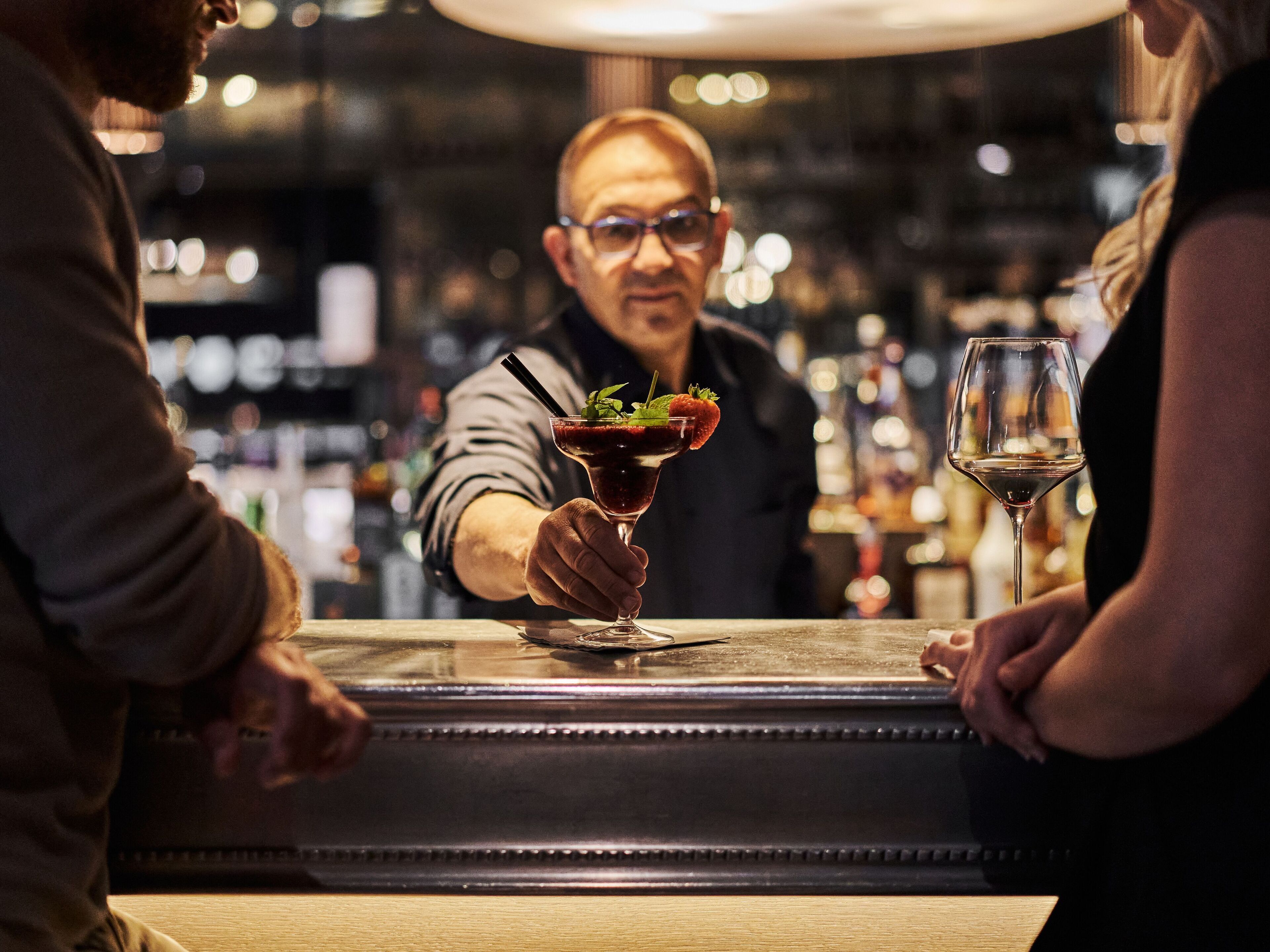 Un barman prépare un cocktail décoré d’une fraise dans un bar.