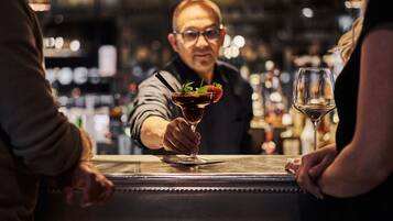 Un barman prépare un cocktail décoré d’une fraise dans un bar.
