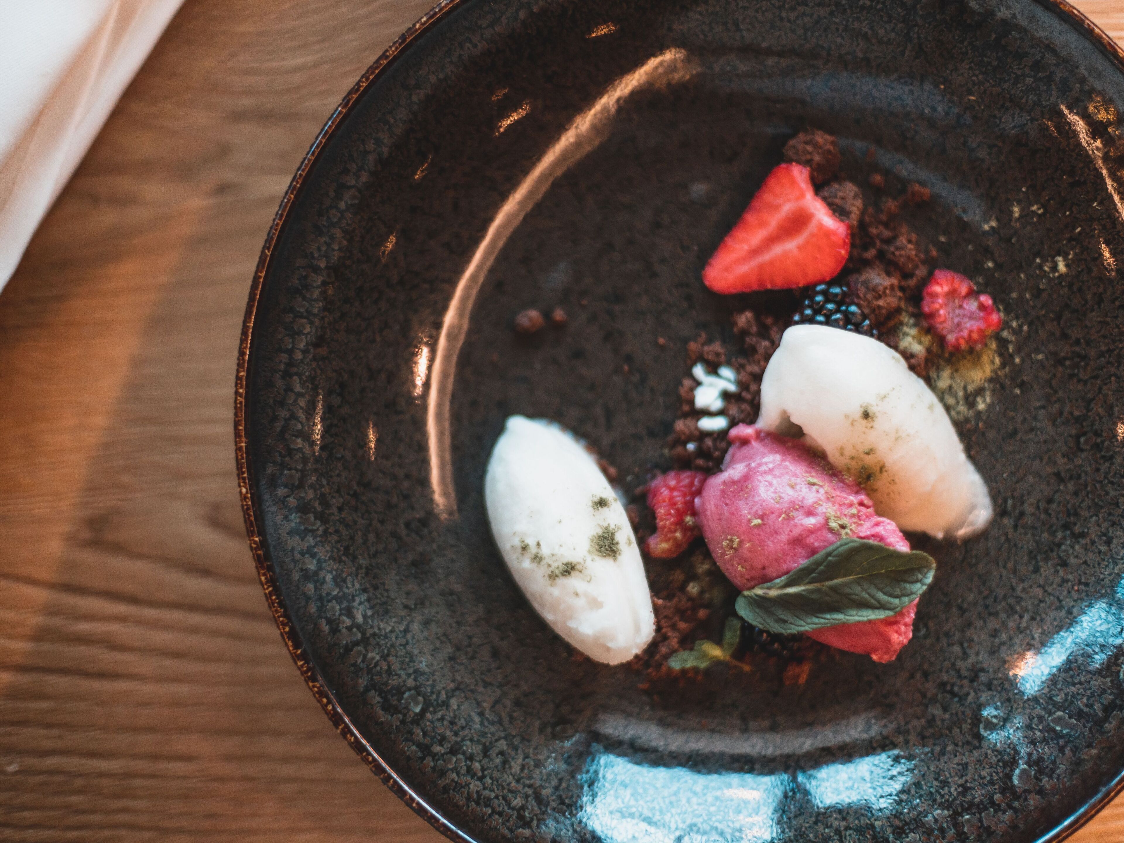 A dessert on a dark plate with strawberries and raspberries.