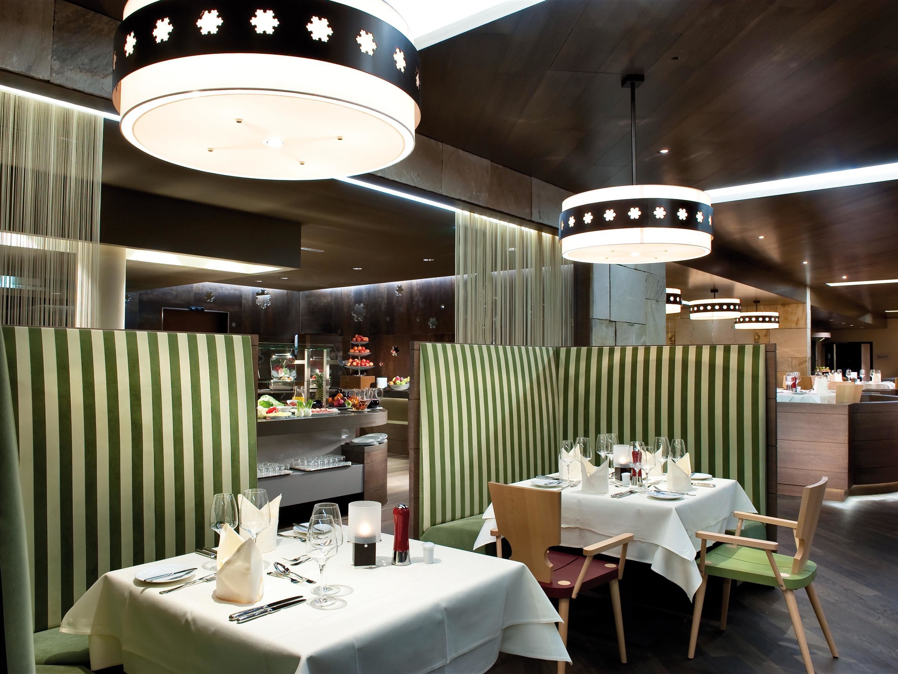 A restaurant with green-striped booths, white tablecloths, and modern pendant lighting.
