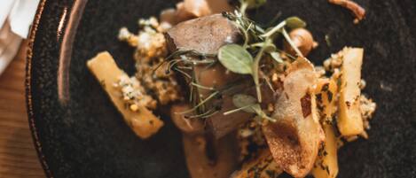 A dark ceramic plate with a food dish, possibly a steak or meat, garnished with herbs and a creamy sauce.