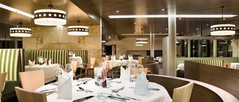 A restaurant with round tables set for dining, featuring white tablecloths and silverware.