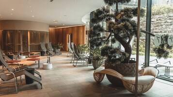 Un espace détente moderne, doté de sièges confortables, d’un grand arbre en pot et offrant une vue sur l’extérieur.