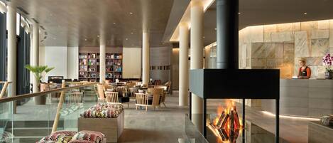 A modern lobby with a central fireplace, seating area, and a library.