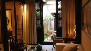Una sala de estar acogedora con un sofá, una mesita de centro y un sillón. Se ve una escalera apoyada en la pared y una ventana con cortinas.
