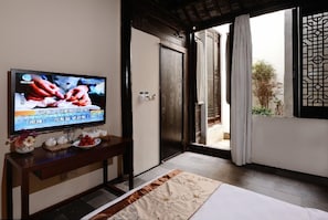 A hotel room with a television on a wooden console, a bed with a patterned bedspread, and a view of the outdoors through a sliding door.