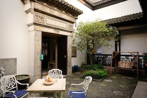 An outdoor seating area with a table and chairs, a tree, and a traditional gate.