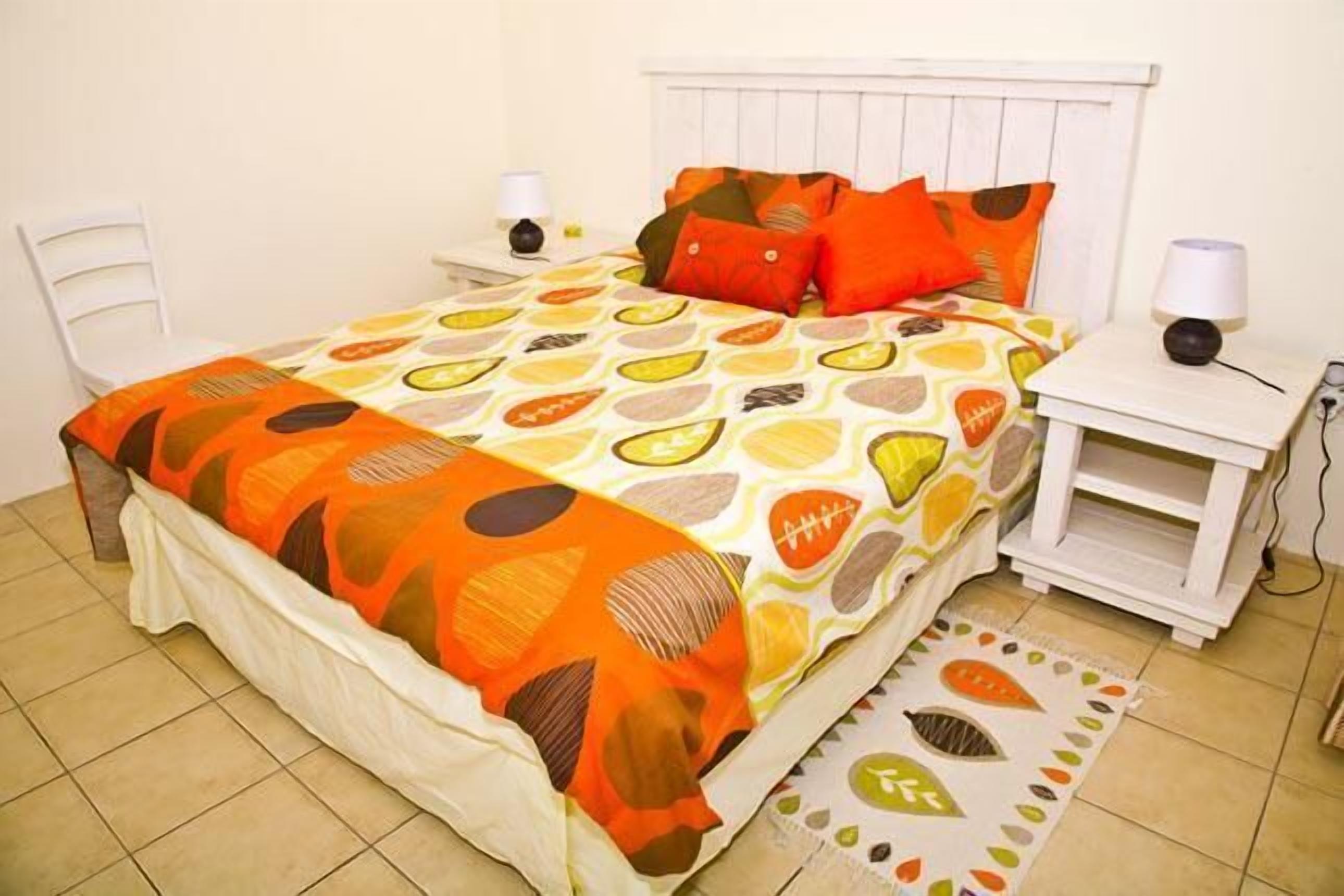 A neatly made bed with a patterned bedspread, a white headboard, and two bedside tables with lamps.
