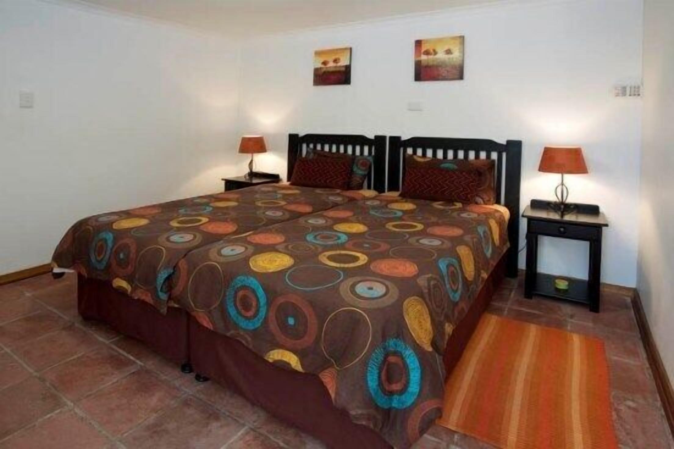 A bedroom with a large bed, two bedside tables with lamps, a patterned bedspread, and two wall-mounted paintings.