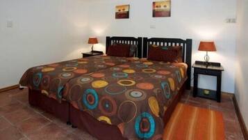 A bedroom with a large bed, two bedside tables with lamps, a patterned bedspread, and two wall-mounted paintings.