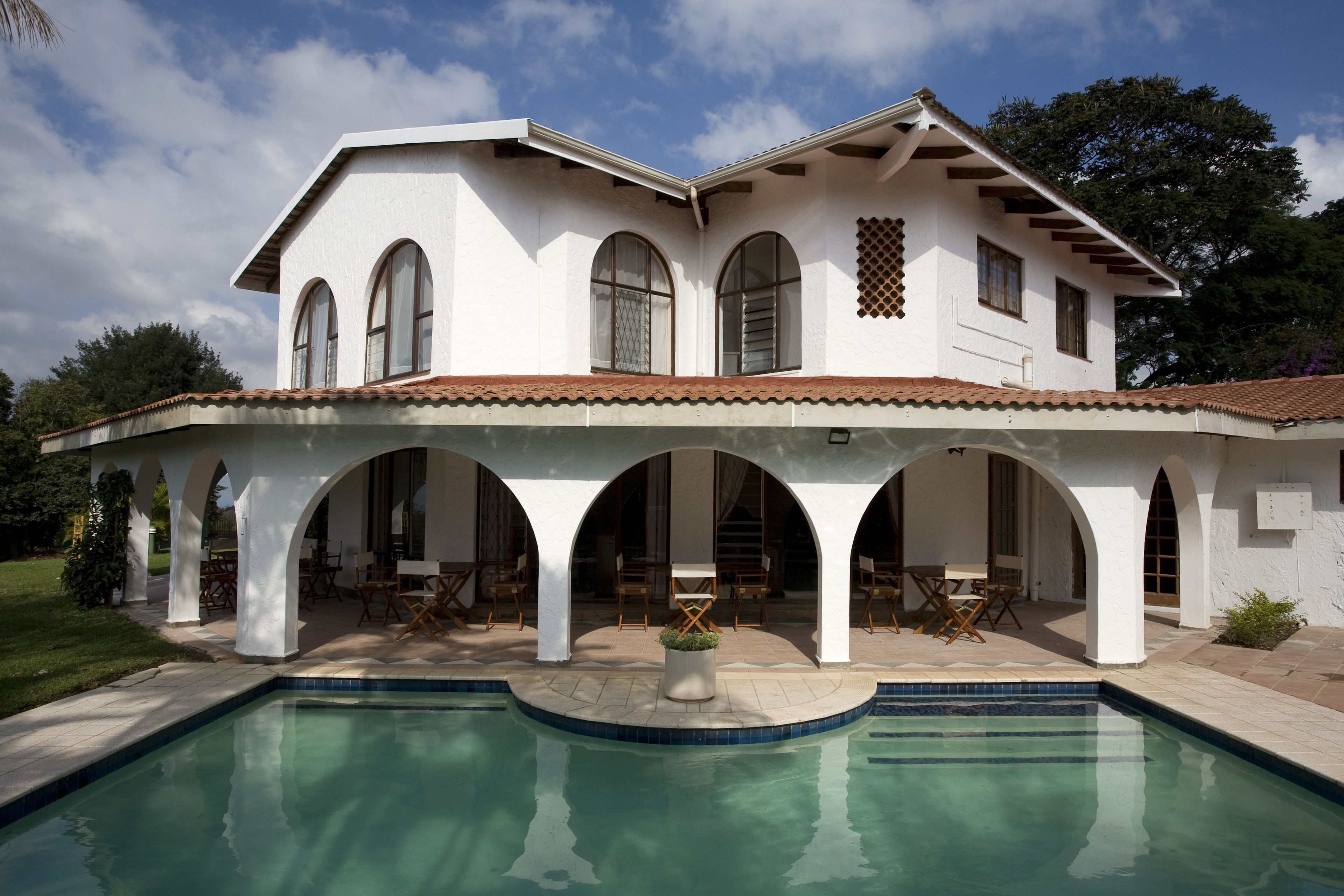 A two-story house with a swimming pool, arched porches, and outdoor furniture.