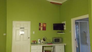 A room with a green wall, a white door, a small white desk with a microwave, a chair, and a television mounted on the wall.