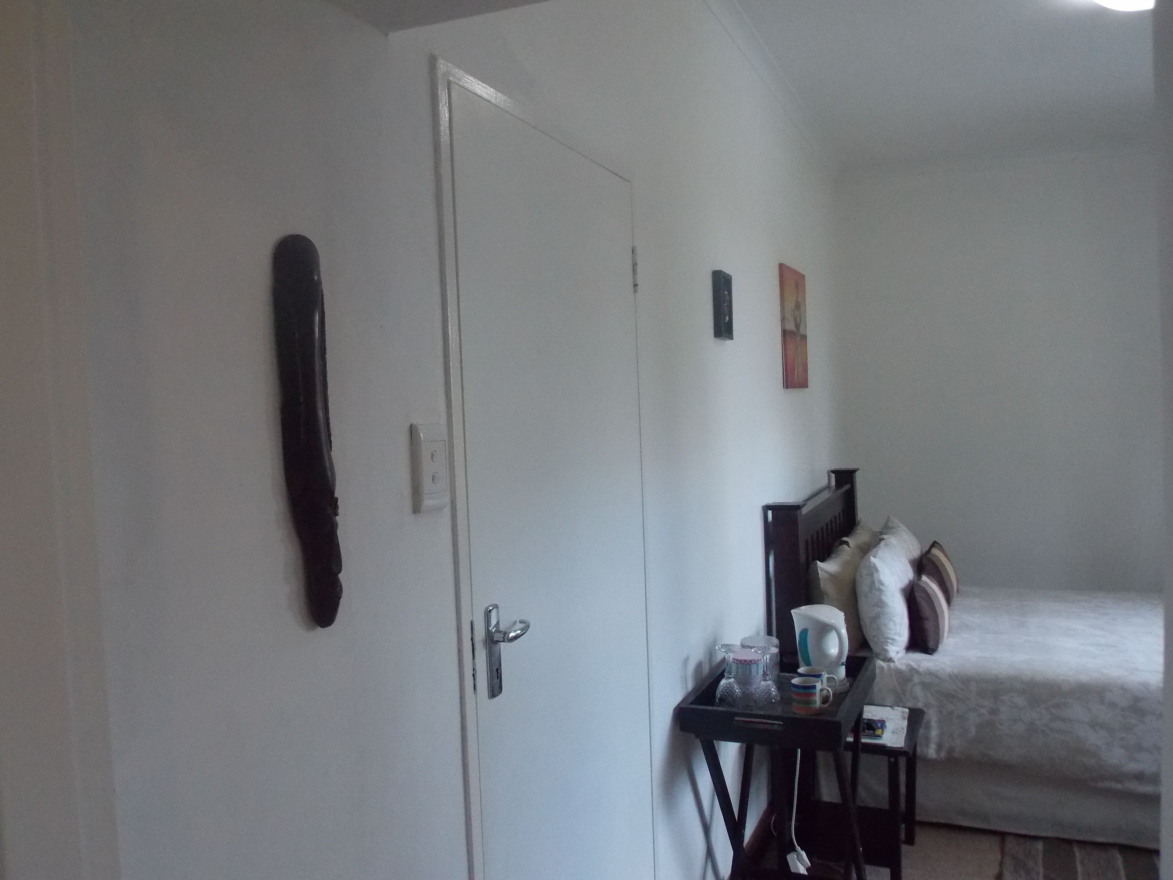 A bedroom with a bed, a nightstand, a door, and a wall-mounted artwork.