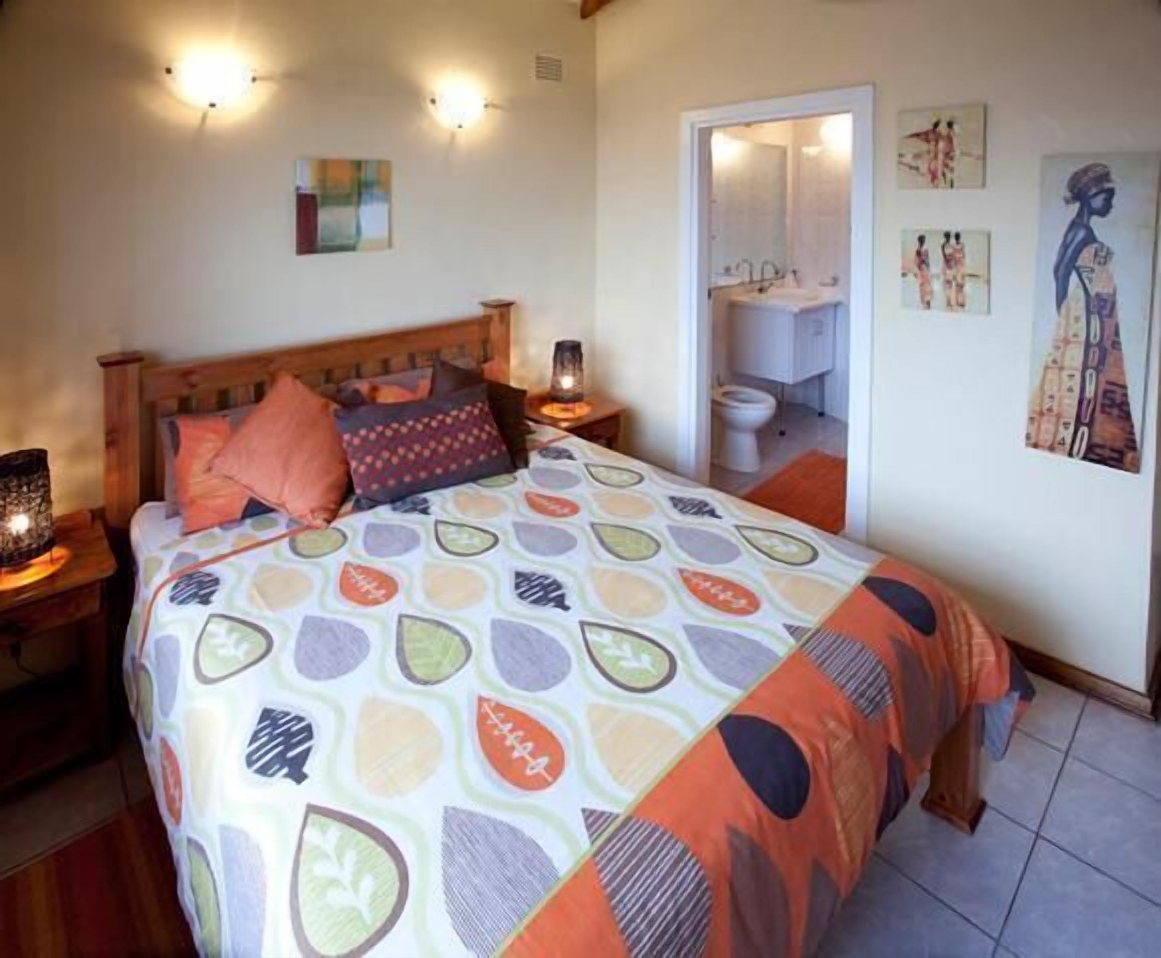 Un dormitorio con cama, mesitas de noche, lámpara de noche, puerta que da a un baño y decoración en la pared.