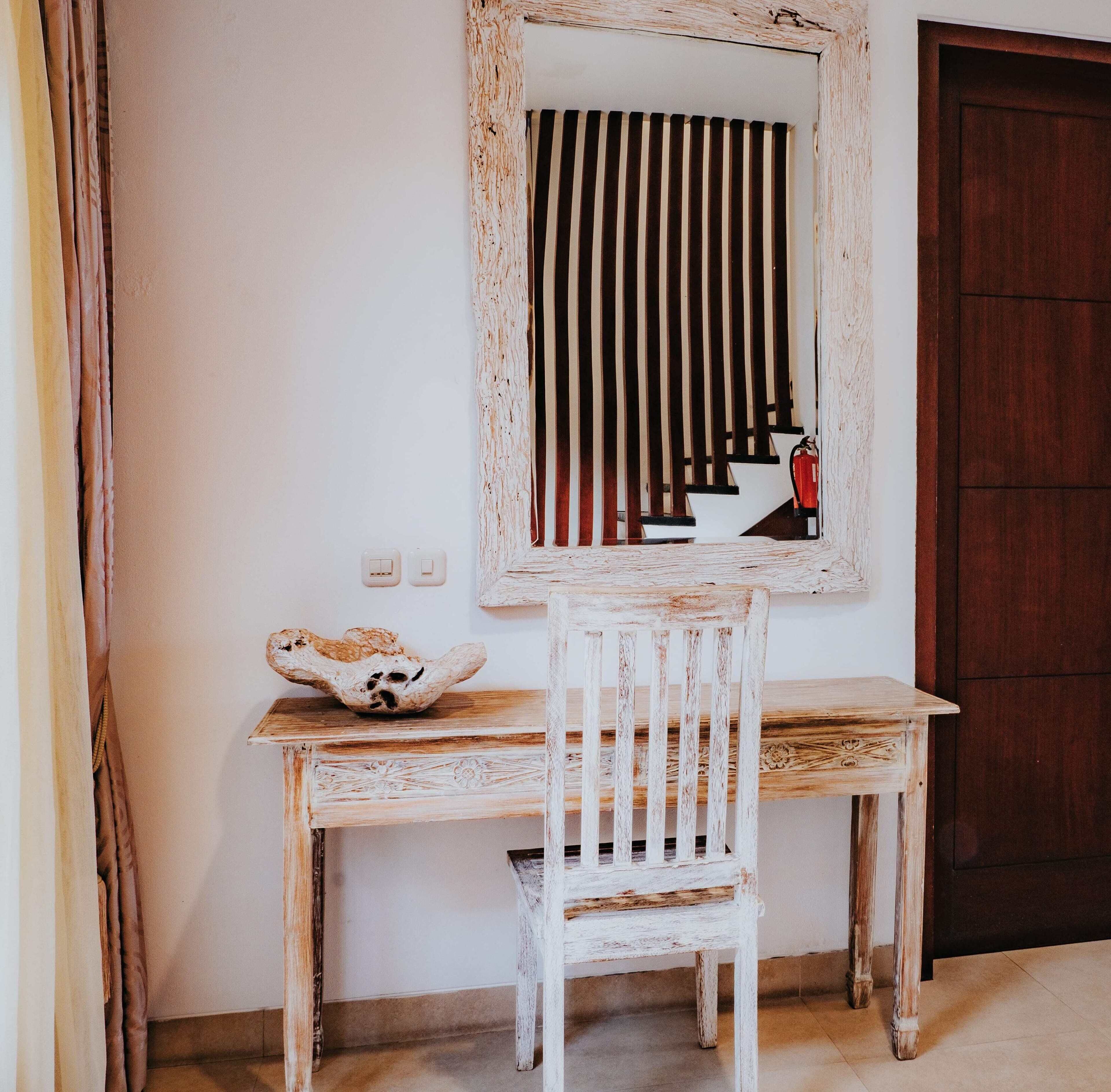 A rustic wooden desk with a white chair, a decorative bowl, and a mirror with vertical stripes.